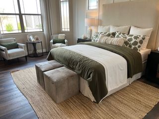 An elegant bedroom featuring plush bedding, sleek furniture, and cozy seating, accented by natural light and rustic elements.