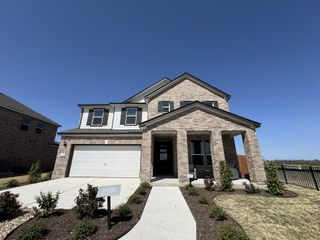 A beautiful brick home with a modern facade and landscaped yard in Mustang Valley by KB Home (Manor, TX).