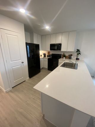 A modern kitchen featuring white cabinetry, black appliances, and sleek countertops with bright lighting and vinyl flooring.