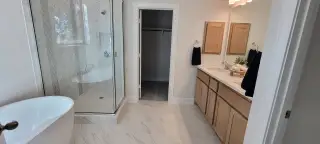 A modern bathroom with a glass shower, elegant bathtub, dual sinks, and wood cabinetry, offering a sleek and functional design.