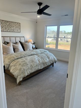 Model Home A cozy bedroom with plush bedding, a ceiling fan, and a large window showcasing scenic views.