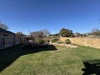 A charming backyard with a stone wall and lush lawn in Blanco Vista by Pacesetter Homes, San Marcos, TX.