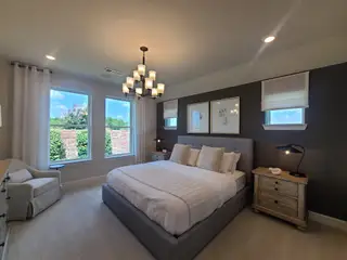 Model Home A cozy bedroom featuring a plush bed, dark accent wall, elegant lighting, and ample natural light from large windows.