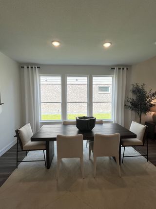 Model Home A modern dining room with a dark wood table, white chairs, and natural light filtering through large windows.