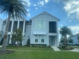 A charming light gray home with a cozy porch and lush landscape in West End at Town Center by ICI Homes (Ponte Vedra, FL).