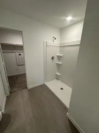 A modern bathroom with a spacious walk-in shower, sleek light fixtures, and wood-inspired flooring.