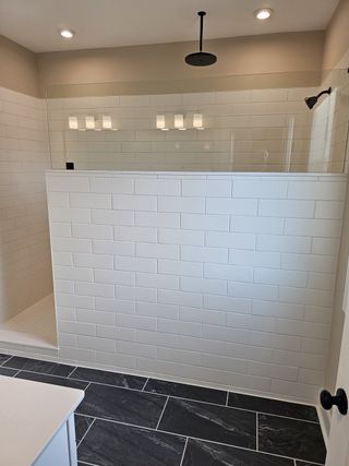 A luxurious walk-in shower with sleek black tile flooring, white subway walls, and a spacious rainfall showerhead.