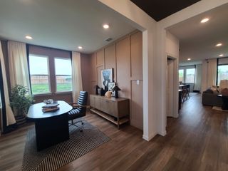 A modern home office with a sleek desk, leather chair, and large windows, complemented by wood flooring and recessed lighting.