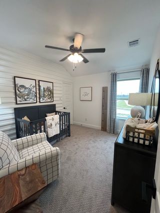 A cozy nursery with a checkered chair, dark crib, and soft carpeting, enhanced by whimsical art and a large window.