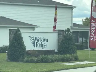 Street view Charming entrance to Seasons at Wekiva Ridge by Richmond American Homes, surrounded by lush greenery in Mount Dora, FL.