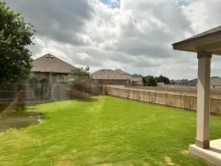 A spacious, fenced backyard in Salerno by KB Home (Round Rock, TX) features lush green grass and a covered patio, perfect for outdoor relaxation.