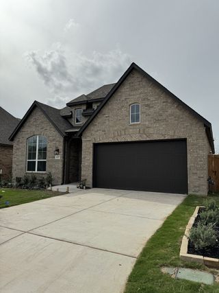 A traditional brick home in VIDA by Highland Homes (San Antonio, TX) features a dark garage door, arched windows, and freshly landscaped grounds.