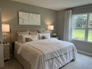 A cozy bedroom with a plush bed, modern art, ambient lighting, and large window overlooking a green backyard.