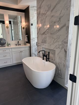 Model Home A luxurious bathroom featuring a sleek freestanding tub, marble accent wall, modern fixtures, and elegant lighting.