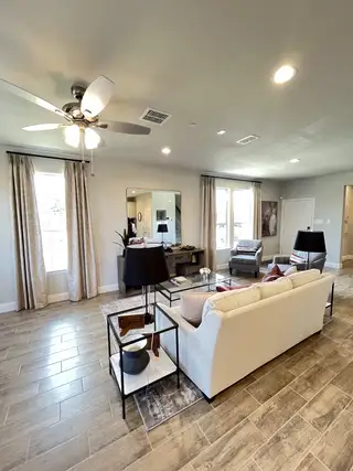 Model Home A spacious living room with a cozy sofa, elegant decor, and wood-style flooring, accentuated by natural light from wide windows.