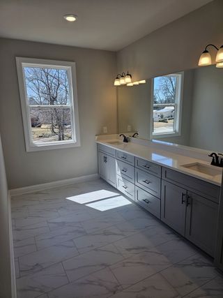 A bright bathroom with a dual-sink vanity, elegant lighting, and sleek marble-tiled floors.