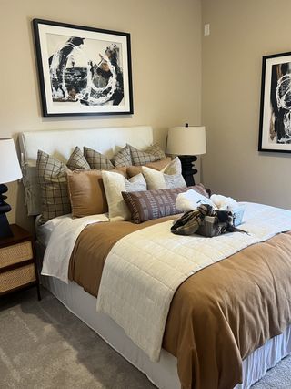 Model Home A cozy bedroom with warm earth-toned bedding, plush pillows, and abstract artwork, creating a stylish and inviting retreat.