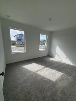 A bright room with plush carpet, two large windows, and ample natural light, offering a cozy atmosphere for relaxation. 