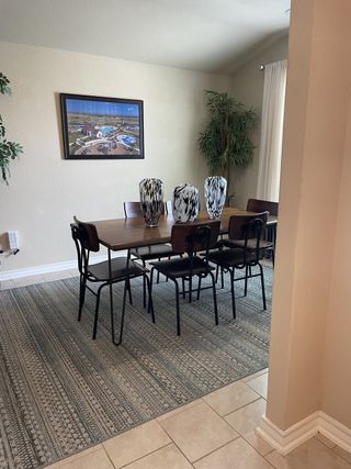 Model Home A simple dining area with a wooden table, black metal chairs, and a patterned rug offers a functional and inviting space.