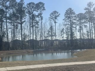 A tranquil pond reflects towering pines in Lindera Preserve at Cane Bay Plantation (Summerville, SC), by Lennar Homes, offering serene community living.