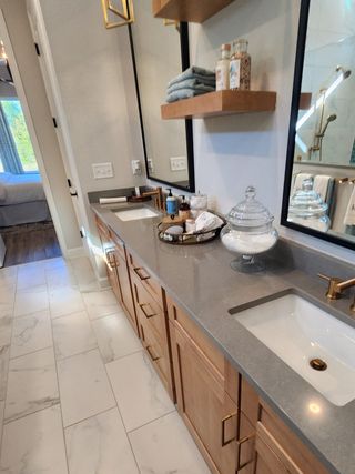 Model Home A luxurious bathroom featuring dual sinks, quartz countertops, and floating wood shelves, blending elegance with function.