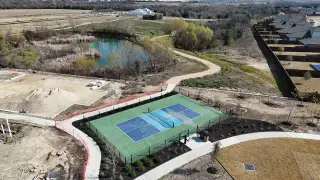 An aerial view of Lisso by Taylor Morrison in Pflugerville, TX, featuring a pickleball court, pond, walking trail, and new home construction, highlighting recreational options.