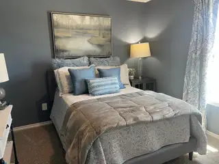 Model Home A cozy bedroom with deep blue walls, a plush bed with patterned pillows, and elegant artwork above the headboard.