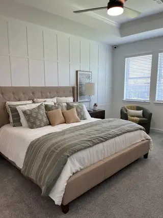 A cozy bedroom with a tufted headboard, stylish pillows, and natural light coming through large windows.