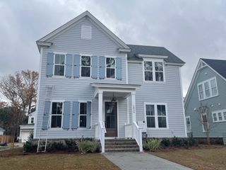 Street view A charming grey home with blue shutters and manicured landscaping in The Settlement at Ashley Hall by Homes by Dickerson (Charleston, SC).