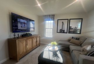 A cozy living room featuring a wall-mounted TV, guitar artwork, and a stylish gray sectional with a sunny ambiance.