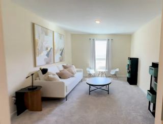 Model Home A cozy living room featuring a white sofa, abstract art, and a round coffee table, complemented by soft carpeting.