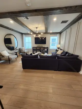 A cozy living room featuring exposed beams, a modern chandelier, and a plush sectional with elegant decor.
