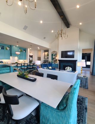A spacious living area with vaulted ceilings, teal accents, a sleek dining table, and elegant chandeliers.