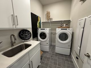 A modern laundry room featuring sleek white cabinetry, stylish tile flooring, and a convenient utility sink.