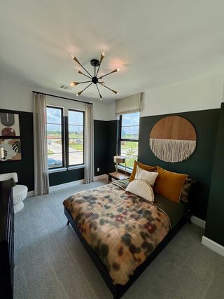 A chic bedroom with dark green walls, modern lighting, plush bedding, and large windows that invite natural light.