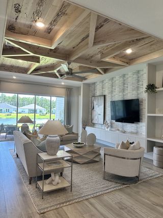A chic living room with a unique wooden ceiling, cozy seating, modern decor, and large windows overlooking the lush outdoors.