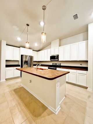 Modern kitchen with white cabinetry, pendant lighting, a sleek countertop, and stainless steel appliances.