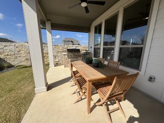 Model Home A cozy patio with a wooden dining set, grill, ceiling fan, and privacy wall, perfect for outdoor gatherings.