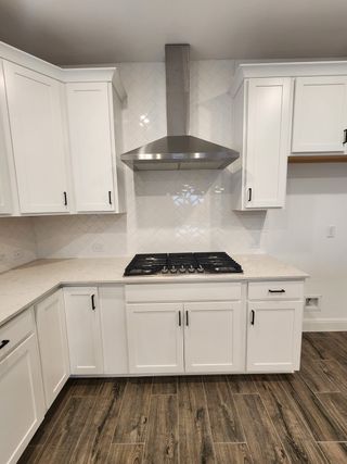 Model Home A modern kitchen with white shaker cabinets, a sleek stainless steel range hood, and wood-look tile flooring.