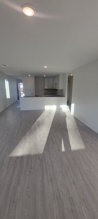 Model Home An open-concept room with sleek, light wood flooring and a modern kitchen featuring white cabinetry.