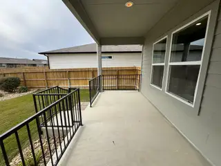 A spacious covered patio with a black metal railing, perfect for outdoor lounging while overlooking a beautifully manicured backyard.