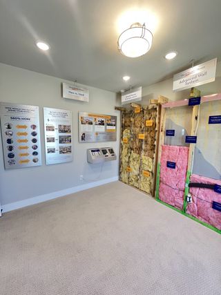 A modern display room showcasing advanced home construction techniques with informational posters and insulated wall samples.