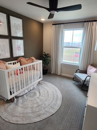A cozy nursery featuring a white crib, playful rabbit art, a neutral rug, and modern ceiling fan with ample natural light.
