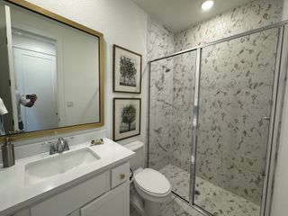 Model Home A stylish guest bathroom with white cabinetry, a gold-framed mirror, and a modern glass shower with hexagonal tile details.