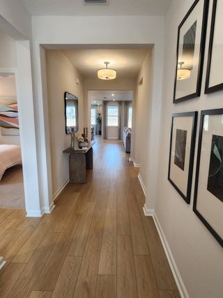 A welcoming hallway with wood floors, modern lighting, and framed art, leading to a spacious living area.