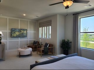 A cozy bedroom with a seating area, modern decor, large windows, and an elegant ceiling fan.