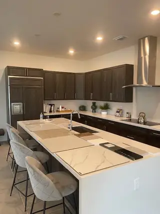 A modern kitchen with dark cabinets, a large marble-topped island, sleek appliances, and stylish seating.