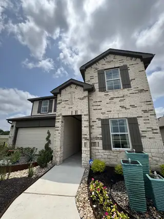 A charming light brick home with dark shutters and landscaped garden in Prairie Lakes by D.R. Horton (Buda, TX).