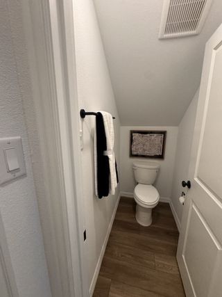 A compact powder room with sleek wood flooring, a minimalist white toilet, and modern black fixtures.