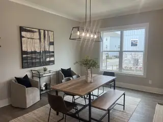 A modern dining room with sleek lighting, a wooden table, abstract art, and cozy armchairs.